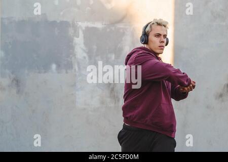 Fitness man warming up outdoors on sports ground and listen to music in headphones. Rotates body and swings hands Stock Photo
