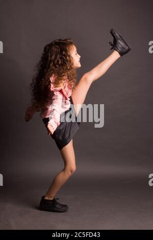 Studio portrait of a little girl, with curly curly hair, in a pink blouse and black shorts, dancing on a dark red background Stock Photo