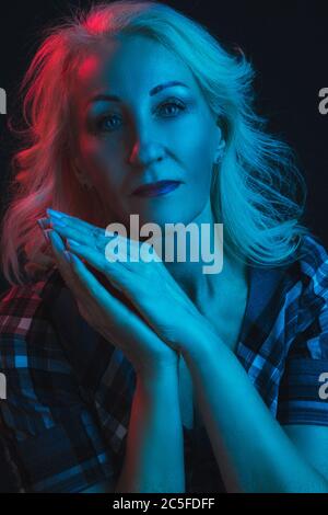 Studio portrait of an elderly blonde with her hands folded palms together gesture at the face, in cold, blue tones Stock Photo