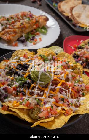 A plate of delicious tortilla nachos with melted cheese sauce, minced meat, jalapeno peppers, red onion, green onions, tomato, black olives, salsa and Stock Photo