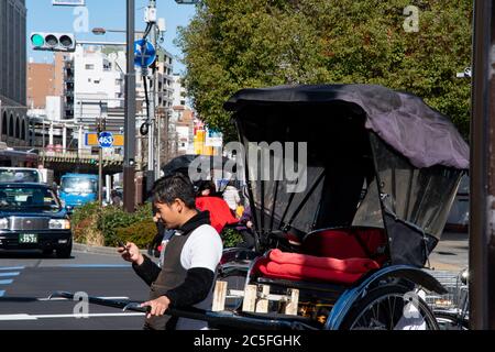 A rickshaw driver looking at his smartphone while stopped at a red traffic light in Asakusa. Traffic on the street.Tokyo, Japan Stock Photo