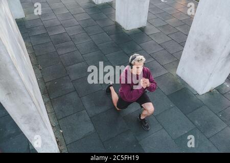 Young athletic man with headphones listen to music and warming up outdoors. Do lunge Stock Photo