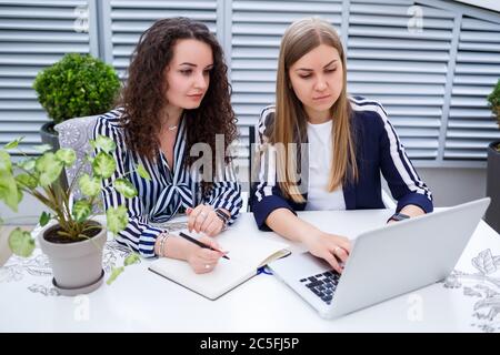 Two successful young business women manager are sitting at a table with a laptop and a notebook working on a new development project, female students Stock Photo