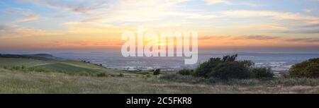 Panoramic view from Ditchling Beacon during sunset, with a dramatic cloudy sky and grass meadows in the foreground. Located on the South Downs Way. Stock Photo