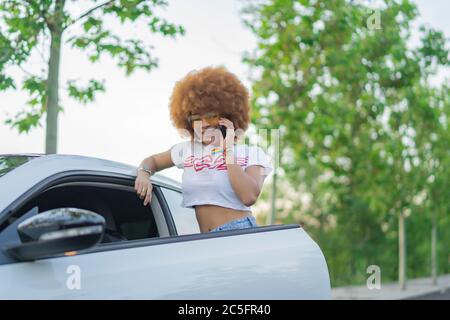 woman with afro hair talking on the phone next to her car Stock Photo