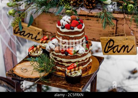 wedding cake with fruit and an old wooden table with decorations and rings during a wedding ceremony in winter on snow in the middle of a forest cover Stock Photo
