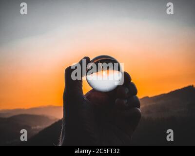 Taking photos of sunset through the small glass ball holding in hand Stock Photo