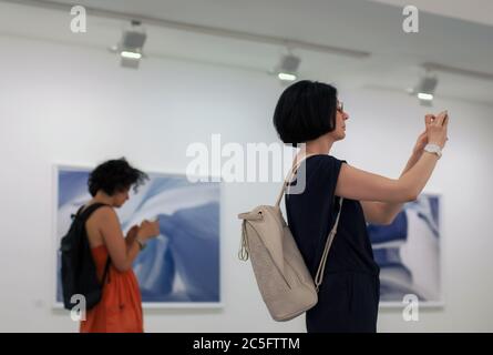 Moscow 11/06/2019 Woman taking pictures at photo exhibition with smartphone, other girl using messenger or social network on her mobile phone, instead Stock Photo
