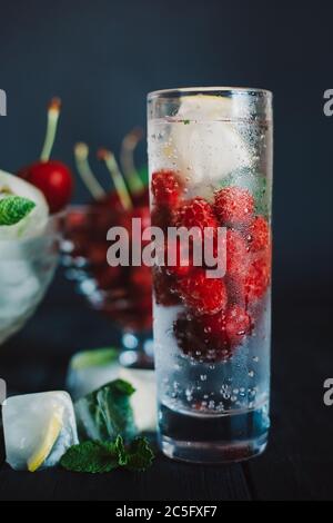 Cold lemonade with raspberries, lemon, ice and cherries on black background Stock Photo