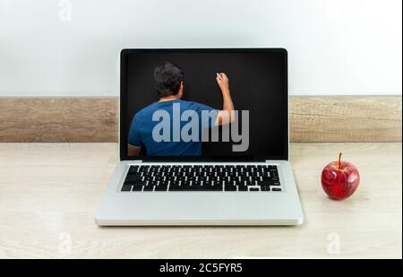 Laptop on a desk with an apple next to it and a teacher on his back writing on a blackboard on his monitor Stock Photo