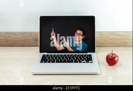 Teacher giving a class in front of a blackboard on the screen of a computer monitor displayed on a laptop on a desk with an apple next to it Stock Photo