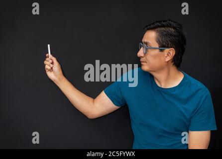 In a class a teacher points to something with chalk on a black board Stock Photo