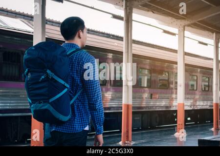 Young asian hipster man standing and waiting train on platform. Stock Photo
