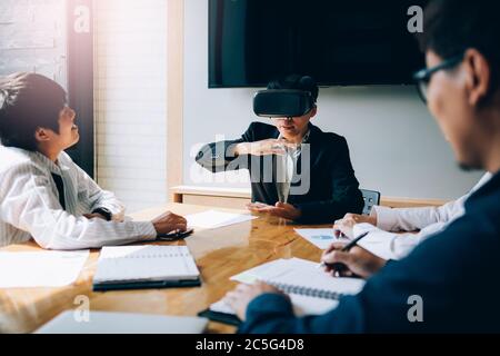 Business team testing virtual reality VR headset technology with colleague in office. Stock Photo