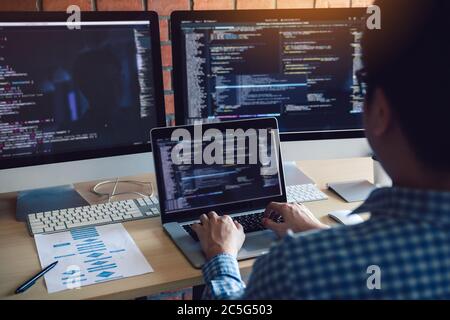 Rear view of software developers is sitting serious analyzing data on the computer screen. Stock Photo
