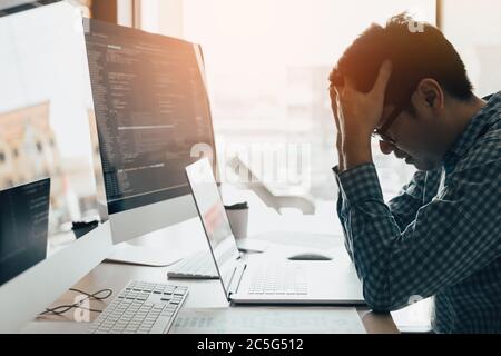 Man programmers are stressed and hand holding head with headache at the office while working analyzing on desk in code at office room. Stock Photo