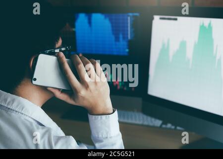 Asian agent trader man working and analysis in office and dealing with market financial charts and graphs and calling to customer. Stock Photo