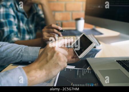 Software developers are using smart phones and analyzing together the code written in the program on the computer. Stock Photo