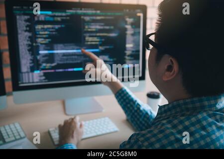 Software developer pointing to the computer screen and is analyzing the code. Stock Photo