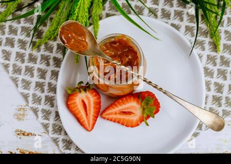 Caramel sauce in glass jar with spoon and sliced strawberry. Top view. Stock Photo