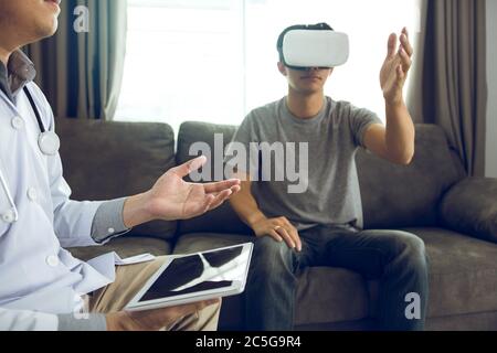 Doctor is using the tablet to send the data to the virtual reality glasses showing the health diagnosis as the patient is wearing and analyzing togeth Stock Photo