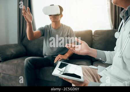 Doctor is using the tablet to send the data to the virtual reality glasses showing the health diagnosis as the patient is wearing and analyzing togeth Stock Photo