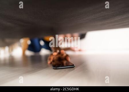 Girl Looking For Lost Mobile Phone Under Sofa Stock Photo