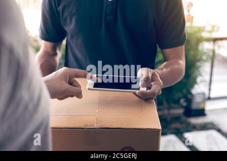 Close up of hand asian man using smartphone pressing screen to sign for delivery from the courier at home. Stock Photo