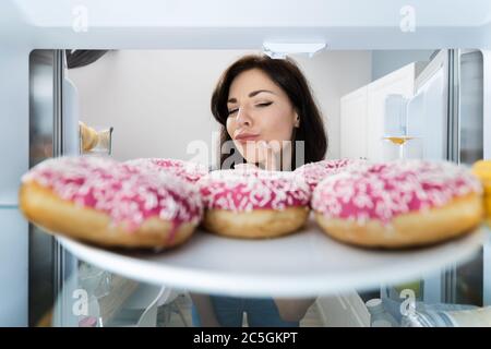 Confused Woman Thinking Looking At Sweets In Fridge Or Refrigerator Stock Photo