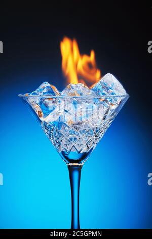 Ice in a martini glass and burning fire on a blue background with reflection and gradient. Stock Photo