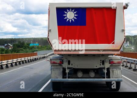 Big  truck with the national flag of  Taiwan  moving on the highway, against the background of the village and forest landscape. Concept of export-imp Stock Photo