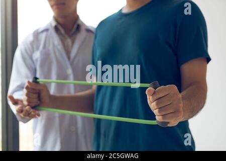 Patient doing stretching exercise with a flexible exercise band and a physical therapist hand to help in clinic room. Stock Photo