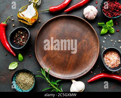 Empty wooden plate and frame of spices, herbs and vegetables on a dark stone background. Top view, flat lay. Stock Photo