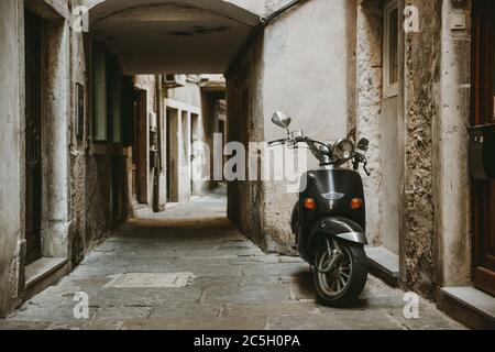 Lonely parked retro scooter in front of one house in old empty narrow alley with stone road of historic town of Piran in Slovenia
