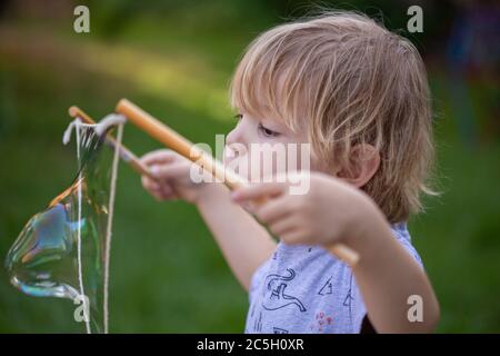 Young preschool boy blowing giant rainbow bubbles in a backyard setting Stock Photo