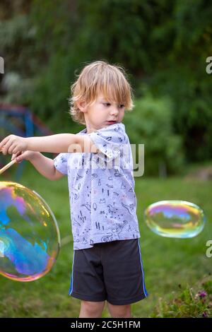 Young preschool boy blowing giant rainbow bubbles in a backyard setting Stock Photo