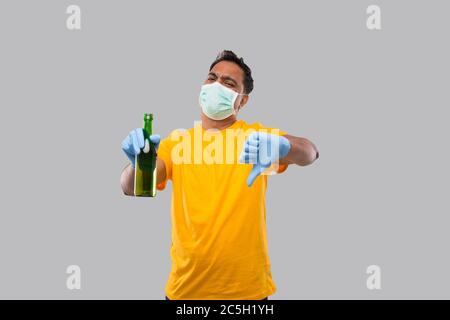 Indian man Holding Beer bottle Showing Thumb Down Wearing Medical Mask and Gloves Isolated. Stock Photo