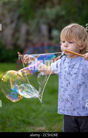 Young preschool boy blowing giant rainbow bubbles in a backyard setting Stock Photo