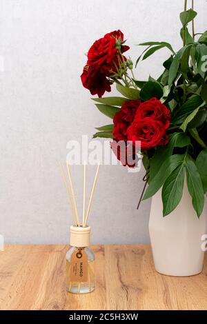 Aroma reed diffuser in the interior. Red rose flowers in vase on wooden table with copy space Stock Photo
