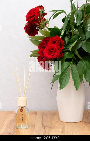 Aroma reed diffuser in the interior. Red rose flowers in vase on wooden table with copy space Stock Photo