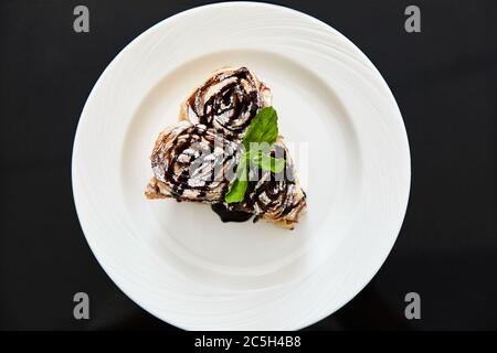 Pie with a piece of greenery. Cake with sprinkles. Dish on black background. Stock Photo