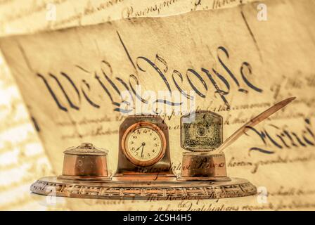 Brown Quill Pen with bronze ink bottle holders with a clock in the middle. Old quill pen writing set, with a transparent United States Declaration of Stock Photo