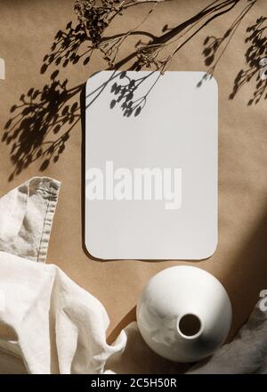 Blank paper sheet on a kraft paper with a ceramic vase and dry grass. Minimalist toned background. Stock Photo