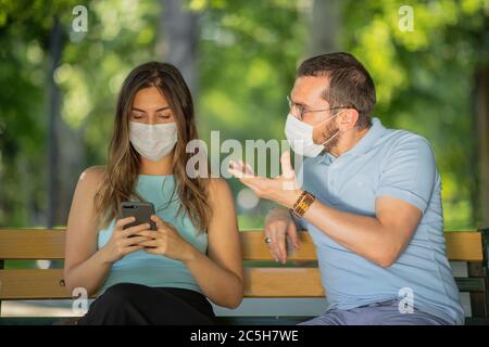 New normal concept after the pandemic an arguing couple view, man is dictating, woman stay cool and unconcerned whie looking mobile phone, they are we Stock Photo