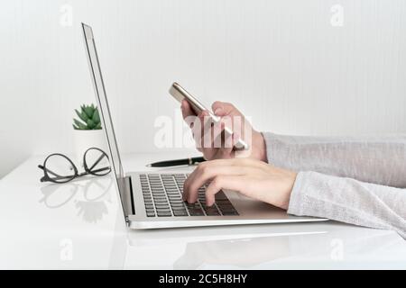 Unrecognizable woman using smartphone while typing on laptop, concept of password entry Stock Photo