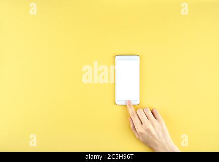 Female hand holding a modern gadget and pointing with finger, on yellow background, top view, copy space Stock Photo