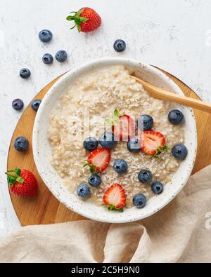 Oatmeal porridge rustic with berries, dash diet, on white wooden background top view Stock Photo