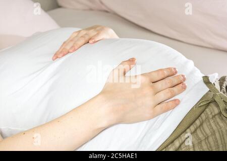 Close shot of pregnant woman’s belly while lying on the bed Stock Photo