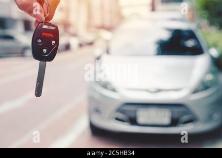 Closeup car key with secutiry remote control button with blur vehicle background for rent drive a car or buy a new car concept. Stock Photo