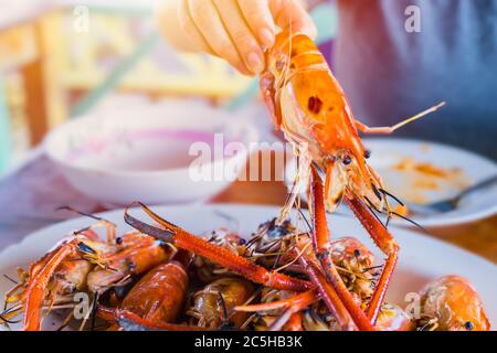 Asian Thai people eating grilled giant river prawn shrimp bbq with spicy sweet and sour seafood dipping sauce yummy popular food in Thailand. Stock Photo